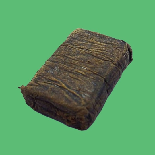 A rectangular, dark brown, wrinkled block of Fendi Hash is displayed against a plain green background.
